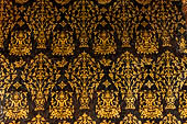 Wat Xieng Thong temple in Luang Prabang, Laos. Detail of the  intricate gold stencilling on black lacquer that decorate the walls of the sim. Floral motifs. 